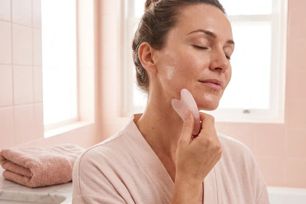 Femme utilisant un gua sha rose le long de la mâchoire, peau huilée
