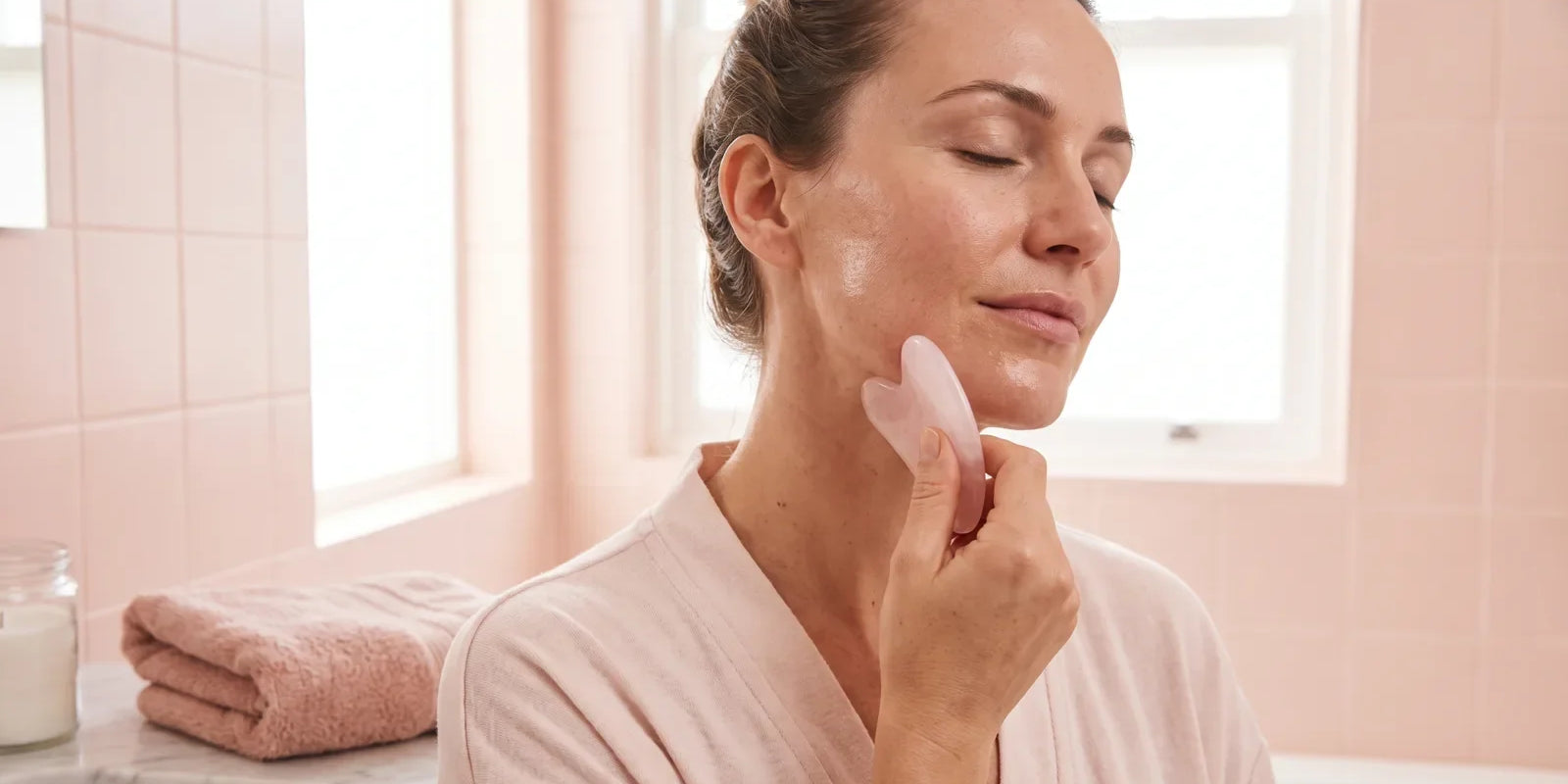 Femme utilisant un gua sha rose le long de la mâchoire, peau huilée