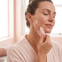 Femme utilisant un gua sha rose le long de la mâchoire, peau huilée