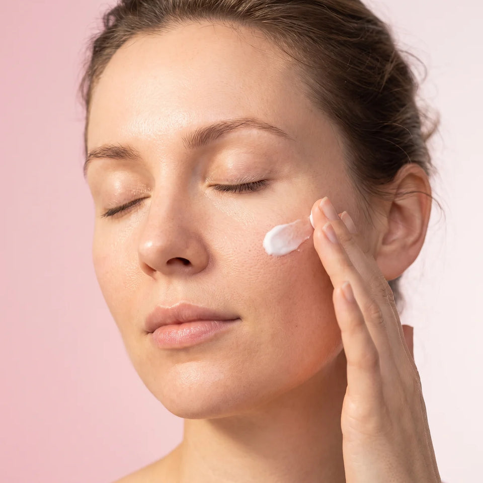 Femme appliquant une crème blanche sur sa pommette, soins visage Glowy