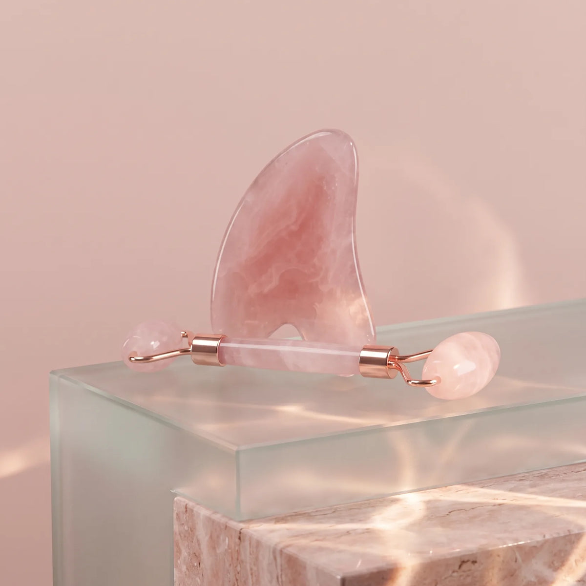Gua sha et rouleau de massage rose posés sur un bloc de verre