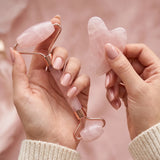 Mains tenant le rouleau visage et le gua sha rose du kit Glowy
