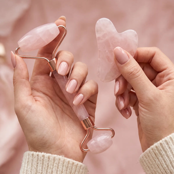 Mains tenant le rouleau visage et le gua sha rose du kit Glowy