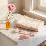 Kit gua sha rose posé dans une salle de bain à côté d'une huile visage