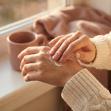 Femme qui applique de la crème sur ses mains sèches, au coin d'une fenêtre