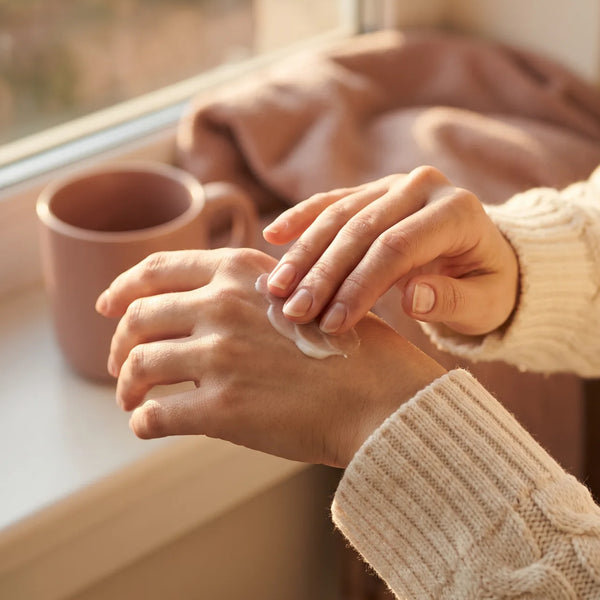 Femme qui applique de la crème sur ses mains sèches, au coin d'une fenêtre