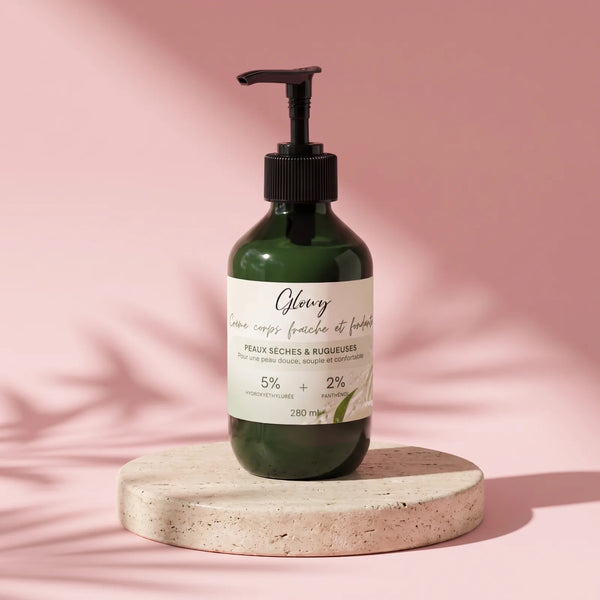 Crème hydratante corps Glowy pour peau très sèche, flacon pompe 280 ml posé sur un socle en pierre