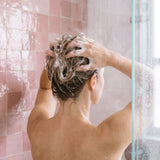 Femme massant le shampoing à la kératine sur les racines de ses cheveux fins sous la douche