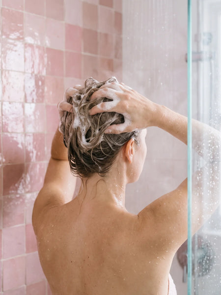 Femme massant le shampoing à la kératine sur les racines de ses cheveux fins sous la douche